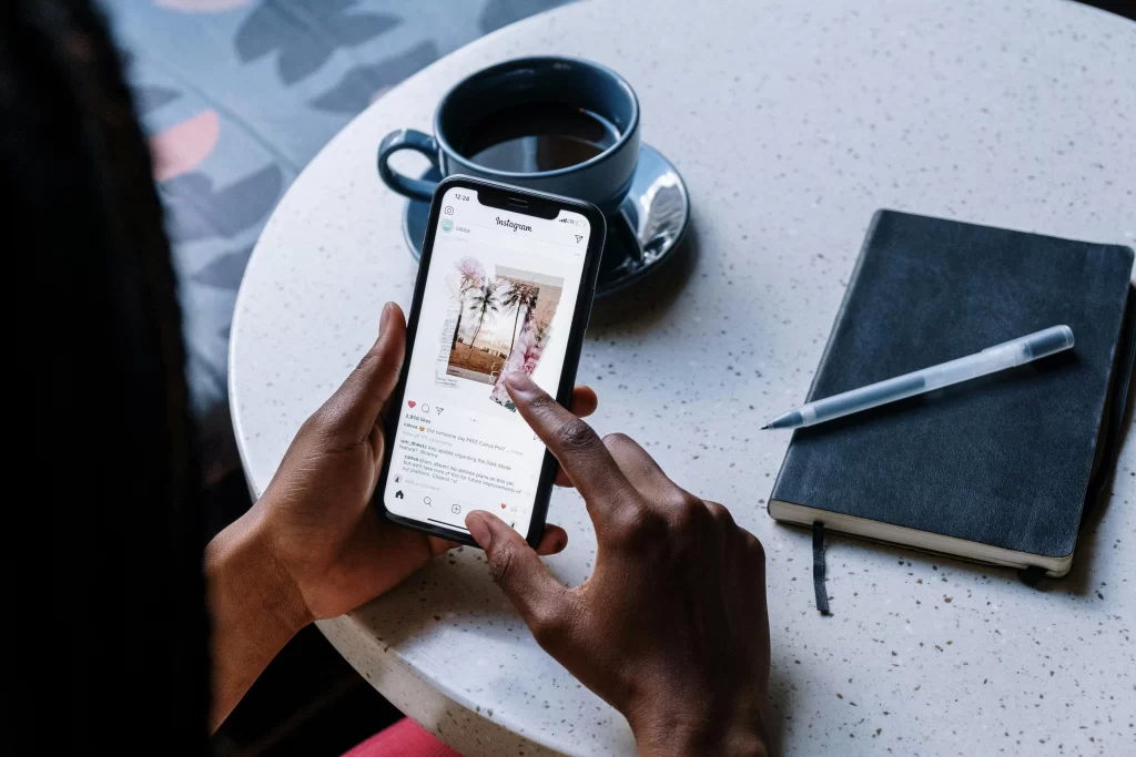 A woman browsing instagram at a table with coffee and a note book